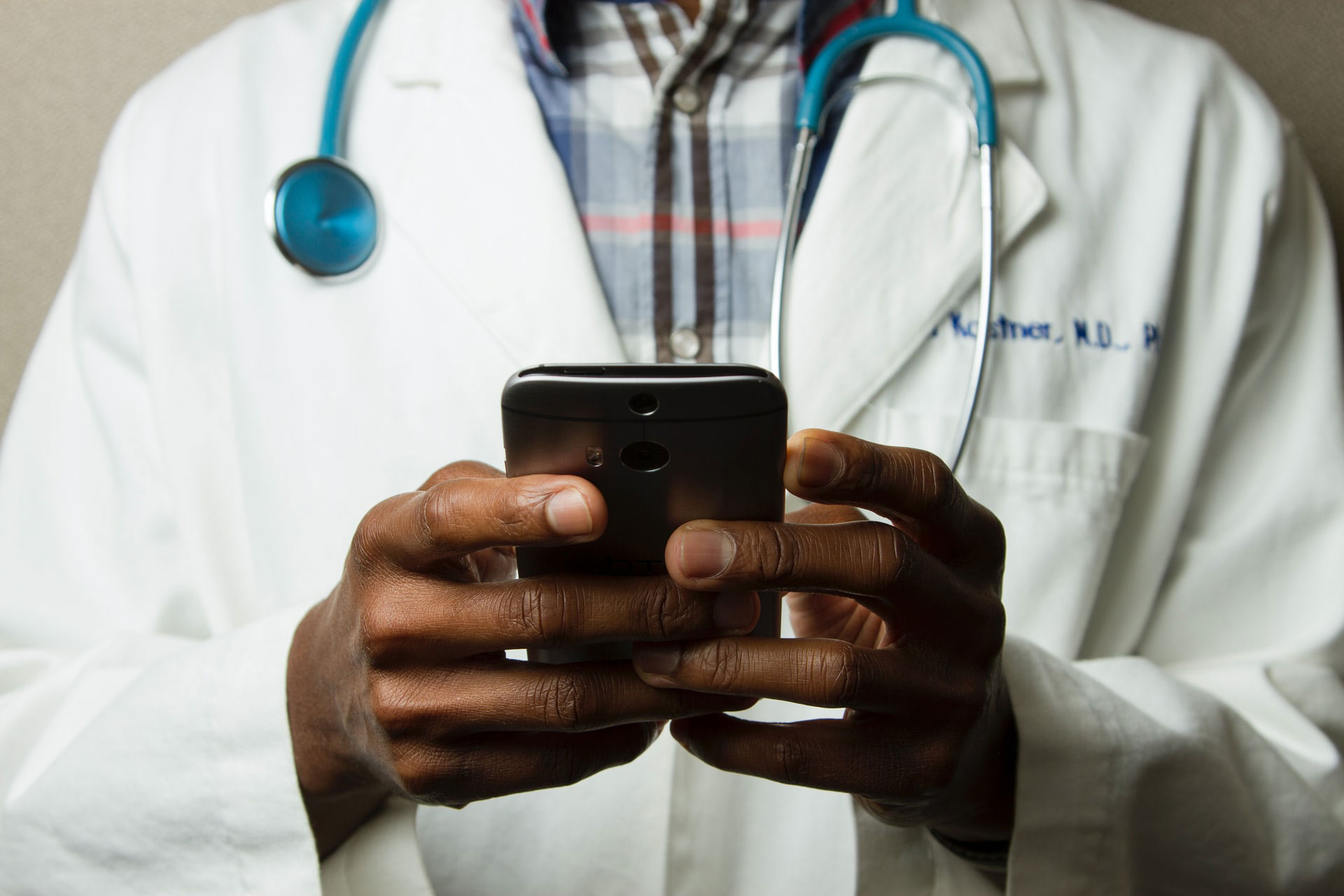 Médico con bata blanca y estetoscopio utilizando un teléfono móvil para consulta o gestión clínica